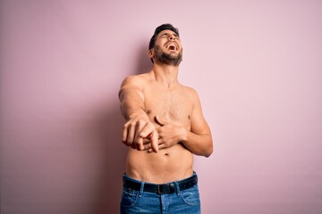 Fototapeta premium Young handsome strong man with beard shirtless standing over isolated pink background laughing at you, pointing finger to the camera with hand over body, shame expression
