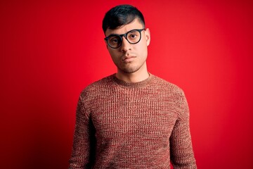 Young handsome hispanic man wearing nerd glasses over red background Relaxed with serious...