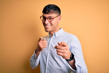 Young handsome hispanic business man wearing nerd glasses over yellow background pointing fingers...