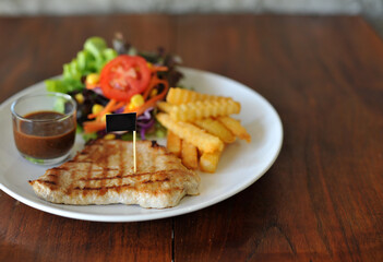 plate of grilled pork steak with french fries and salad on wood background