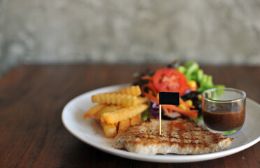 plate of grilled pork steak with french fries and salad on wood background