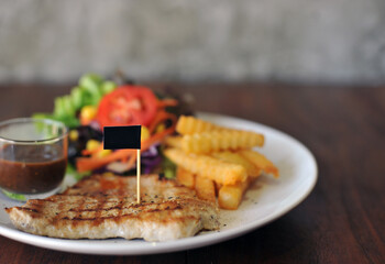 plate of grilled pork steak with french fries and salad on wood background