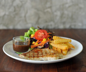 plate of grilled pork steak with french fries and salad on wood background