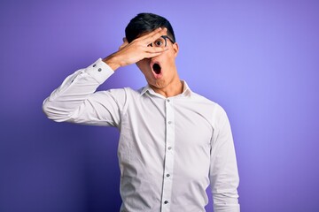 Young handsome business man wearing shirt and glasses over isolated purple background peeking in shock covering face and eyes with hand, looking through fingers with embarrassed expression.