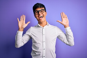 Young handsome business man wearing shirt and glasses over isolated purple background showing and pointing up with fingers number ten while smiling confident and happy.