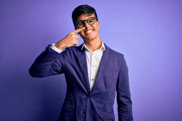 Young handsome business man wearing jacket and glasses over isolated purple background Pointing with hand finger to face and nose, smiling cheerful. Beauty concept