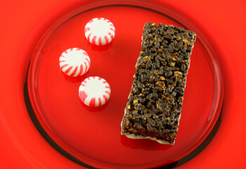 Peppermint chocolate nutrition bar with icing and three peppermint hard candies on red plate