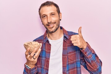 Young handsome man holding cornflakes smiling happy and positive, thumb up doing excellent and approval sign