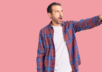 Fototapeta premium Young handsome man wearing casual clothes pointing with finger surprised ahead, open mouth amazed expression, something on the front
