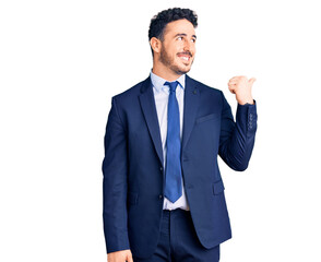 Young hispanic man wearing business clothes smiling with happy face looking and pointing to the side with thumb up.