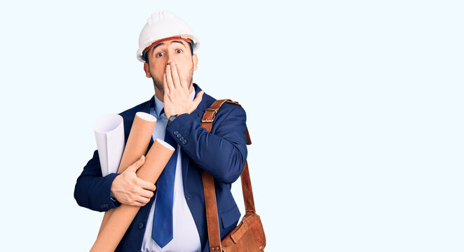 Young hispanic man wearing architect hardhat and leather bag holding blueprints covering mouth with hand, shocked and afraid for mistake. surprised expression