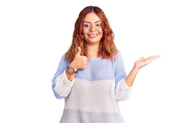 Young latin woman wearing casual clothes showing palm hand and doing ok gesture with thumbs up, smiling happy and cheerful