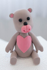 Teddy bear with pink heart cake topper, cute edible decoration made out of colorful sugar paste or fondant icing ready to place on a cake, usual dessert for baby showers, birthdays or special occasion