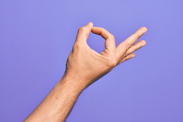 Hand of caucasian young man showing fingers over isolated purple background gesturing approval expression doing okay symbol with fingers