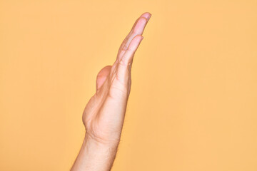 Hand of caucasian young man showing fingers over isolated yellow background showing side of stretched hand, pushing and doing stop gesture