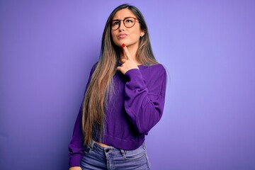 Young beautiful smart woman wearing glasses over purple isolated background Thinking concentrated about doubt with finger on chin and looking up wondering