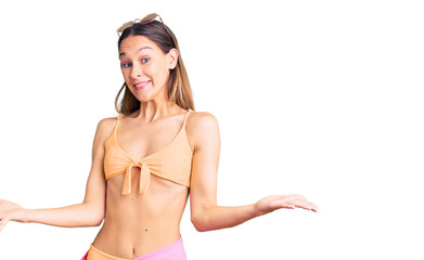 Beautiful brunette young woman wearing bikini and sunglasses clueless and confused expression with...