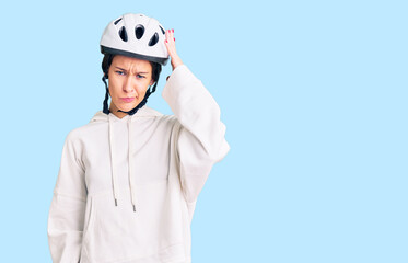 Beautiful brunette young woman wearing bike helmet and sporty clothes confuse and wonder about question. uncertain with doubt, thinking with hand on head. pensive concept.