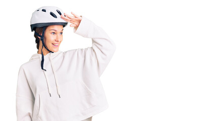 Beautiful brunette young woman wearing bike helmet and sporty clothes very happy and smiling looking far away with hand over head. searching concept.