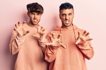 Young gay couple wearing casual clothes smiling funny doing claw gesture as cat, aggressive and sexy expression
