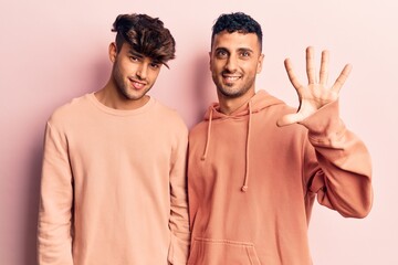 Young gay couple wearing casual clothes showing and pointing up with fingers number five while smiling confident and happy.