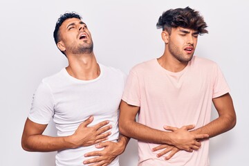 Young gay couple wearing casual clothes with hand on stomach because nausea, painful disease feeling unwell. ache concept.