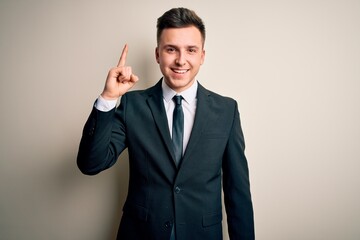 Young handsome business man wearing elegant suit and tie over isolated background showing and pointing up with finger number one while smiling confident and happy.