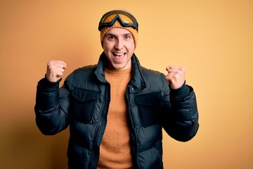 Young handsome caucasian man wearing hat, coat and ski glasses for winter and snow weather celebrating surprised and amazed for success with arms raised and open eyes. Winner concept.