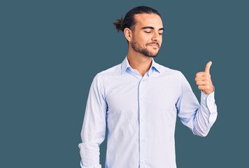 Young handsome man wearing business clothes looking proud, smiling doing thumbs up gesture to the side