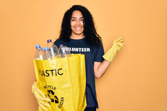 Young african american woman doing volunteering recycling holding bag with plastic bottles very happy pointing with hand and finger to the side