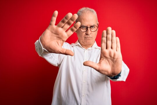 Middle age handsome hoary man wearing casual shirt and glasses over red background doing frame using hands palms and fingers, camera perspective