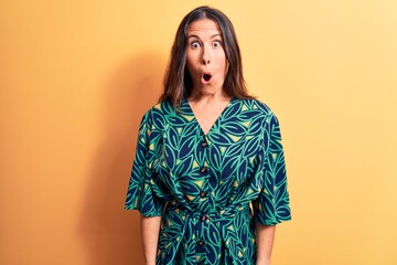 Obraz premium Young beautiful brunette woman wearing casual floral dress standing over yellow background afraid and shocked with surprise expression, fear and excited face.