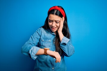 Young brunette woman wearing casual denim shirt over blue isolated background Looking at the watch time worried, afraid of getting late
