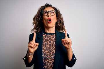 Middle age brunette business woman wearing glasses standing over isolated white background amazed and surprised looking up and pointing with fingers and raised arms.