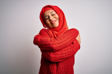 Middle age brunette woman wearing muslim traditional hijab over isolated white background Hugging...