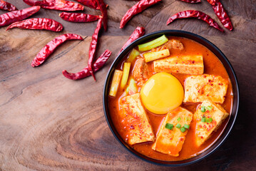 Kimchi soup with tofu, pork and egg yolk in a bowl on wooden background, Korean food (Kimchi Jjigae)