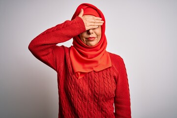 Middle age brunette woman wearing muslim traditional hijab over isolated white background covering eyes with hand, looking serious and sad. Sightless, hiding and rejection concept