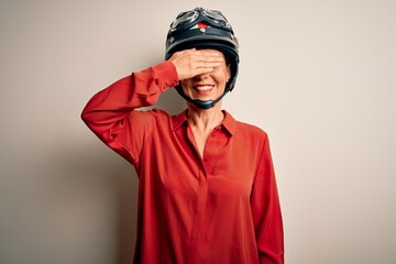 Middle age motorcyclist woman wearing motorcycle helmet over isolated white background smiling and laughing with hand on face covering eyes for surprise. Blind concept.