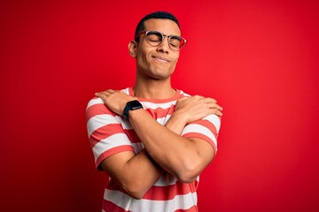 Young handsome african american man wearing casual striped t-shirt and glasses Hugging oneself happy and positive, smiling confident. Self love and self care