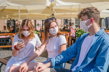 Friends wearing face masks talking and using their smartphones outdoors