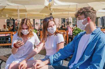 Naklejka premium Friends wearing face masks talking and using their smartphones outdoors