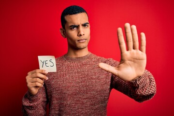 Young handsome african american man holding reminder paper with yes message with open hand doing...