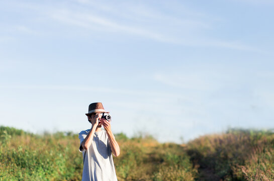 Tourist or photographer with hat taking pictures of a grassy field with an old camera