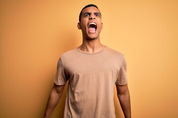 Obraz premium Young handsome african american man wearing casual t-shirt standing over yellow background angry and mad screaming frustrated and furious, shouting with anger. Rage and aggressive concept.