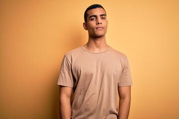 Young handsome african american man wearing casual t-shirt standing over yellow background looking sleepy and tired, exhausted for fatigue and hangover, lazy eyes in the morning.