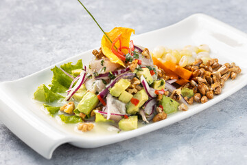 Top shot of a white fish ceviche accompanied with avocado served on a white plate, isolated against a textured rustic gray wood background.