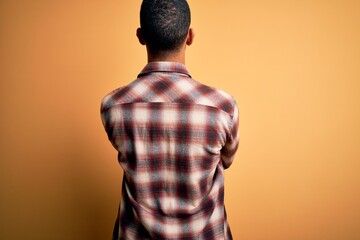 Young handsome african american man wearing casual shirt standing over yellow background standing...
