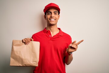 Young handsome african american delivery man holding paper bag with takeaway food very happy pointing with hand and finger to the side