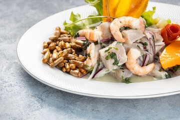 Top shot of a white fish and shrimp ceviche, served on a white plate, isolated against a rustic rustic gray wood background.