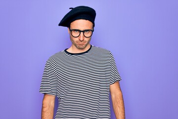 Handsome man with blue eyes wearing striped t-shirt and french beret over purple background skeptic and nervous, frowning upset because of problem. Negative person.